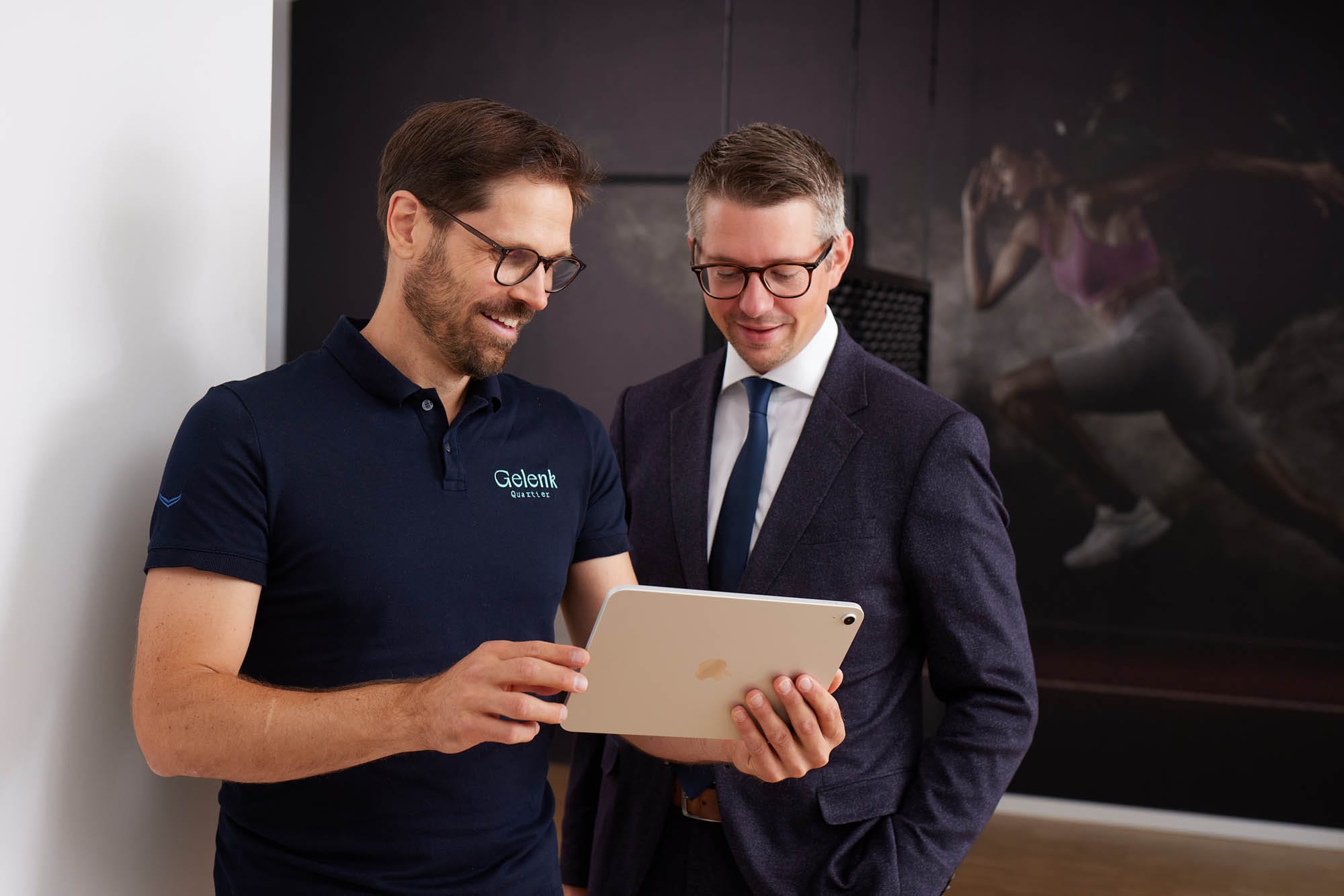 Dr. Nietschke und ein Mann im Anzug stehen nebeneinander. Beide betrachten ein Tablet und sind in ein Gespräch vertieft.