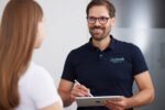 Dr. Nietschke trägt ein dunkelblaues Poloshirt und spricht mit einer Patientin während er Notizen auf dem Tablet macht.