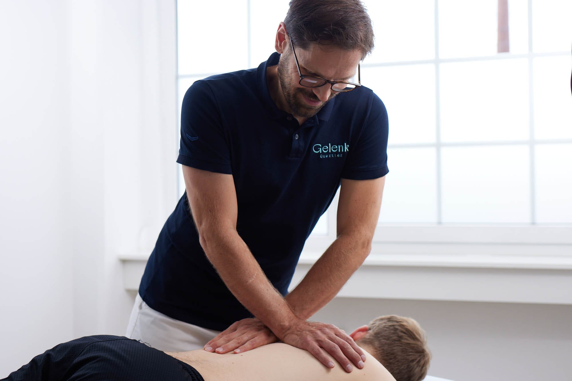 Dr. Nietschke führt eine manuelle Behandlung am Rücken eines liegenden Patienten durch. Er übt Druck mit beiden Händen aus.