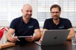 Dr. Zimmerer und Dr. Nietschke sitzen gemeinsam am Tisch. Sie besprechen etwas an einem Laptop und Tablet.
